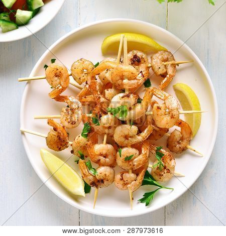 Grilled Shrimp Skewers. Prawns Skewers With Greens, Spices And Lemon On White Plate Over Wooden Tabl