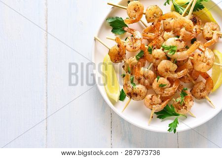 Close Up Of Grilled Shrimp Skewers. Prawns Skewers With Greens, Spices And Lemon On White Plate Over