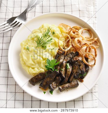 Close Up Of Fried Pieces Of Beef Liver With Mashed Potatoes And Fried Onion Rings On White Plate. Pi