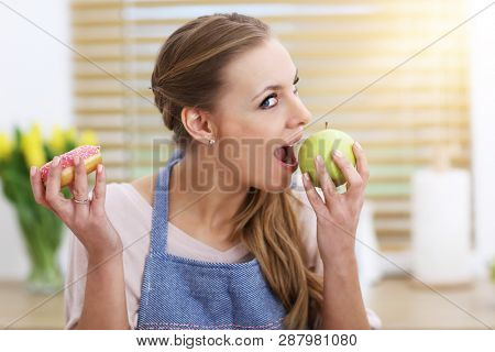 Adult woman choosing between apple and donut in the kitchen
