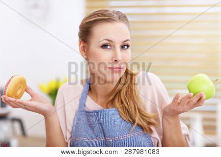 Adult woman choosing between apple and donut in the kitchen