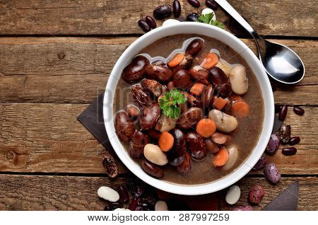 Close-up Of Full Bowl Of Hot Bean Soup With Large Beans On Cutting Board, Carrots, Parsley, Marjoram