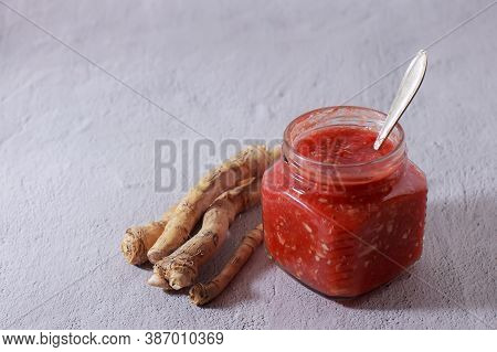 Spicy Appetizer With Tomatoes, Garlic And Horseradish In A Transparent Jar. The Roots Of Horseradish