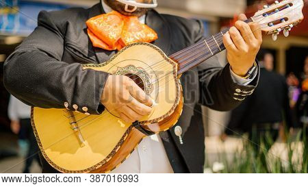Mariachi Playing A Mexican Vihuela With Blurry Pedestrians As Background