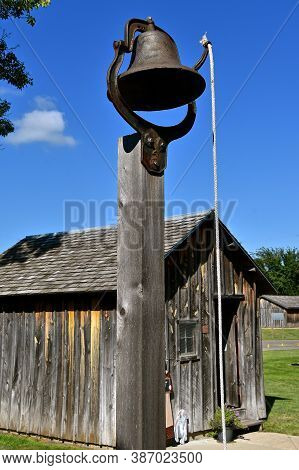 A Cast Iron Bell With A Pull Rope Is Located I Front Of An Old Historic Restored Old One Room School