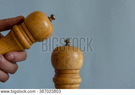Two Peppermills And A Hand On A Blue Background. Wooden Kitchen Utensils For Salt And . Close-up. Se