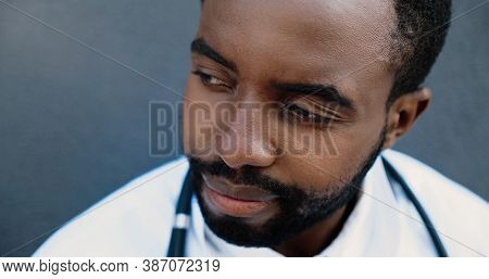 Tired Young Sad African American Man Doctor Taking Off Medical Mask And Resting While Leaning On Wal