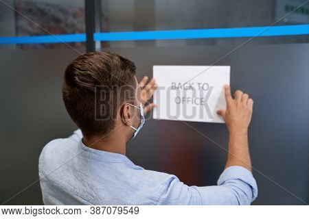 Rear View Of A Young Man, Office Worker Wearing Protective Face Mask Sticking Open Sign With Text Ba