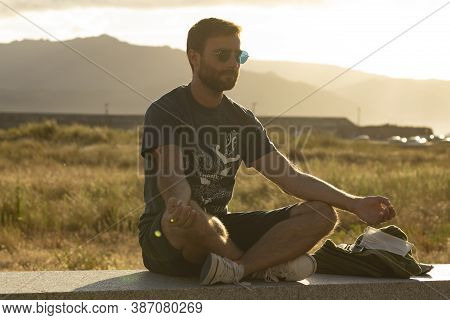 A Young Man, Wearing Glasses, Meditates In A Yoga Posture, While Enjoying The Afternoon Sun On A Pro