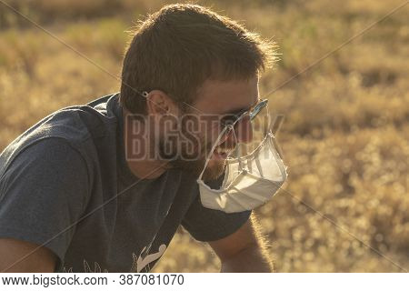 A Young Man Laughs Foolishly, As He Hangs His Protective Face Mask From His Sunglasses.