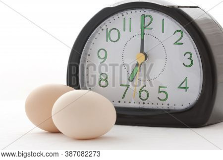 Two Eggs Along With Clock Showing Time 7am, A Breakfast Time On Isolated White Background.