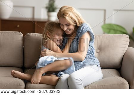 Little Daughter And Young Mommy Hugging On Couch