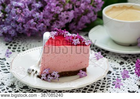 A Berry Mousse Cake With Chocolate Base And Juice Jelly, Decorated With Lilac Flowers, Served With C