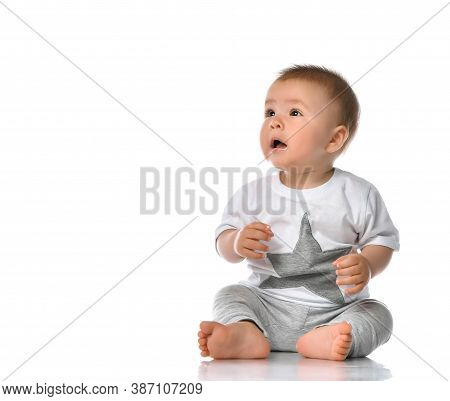 Little Boy Sits In A White Studio On The Floor, Wearing A Gray T-shirt With A Star