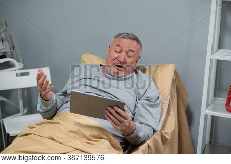 A Senior Man Watching Sports Games On His Tab In A Nurcing Home.