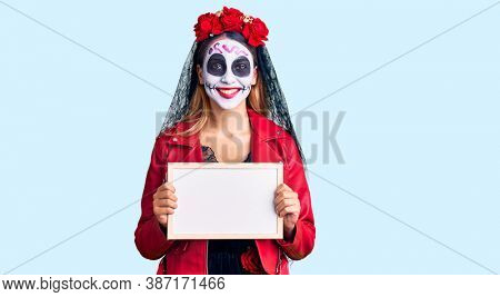 Woman wearing day of the dead costume holding empty white chalkboard looking positive and happy standing and smiling with a confident smile showing teeth 