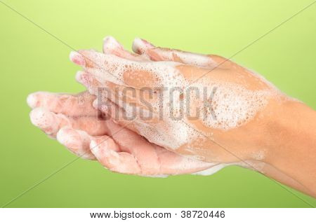 ผู้หญิงมือใน soapsuds บนพื้นหลังสีเขียวอย่างใกล้ชิด