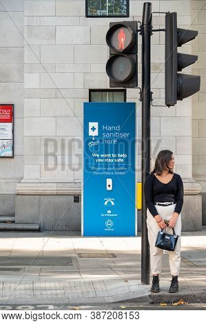 London - September 12, 2020: Woman Stood Waiting At Pedestrian Crossing With Free Public Hand Saniti