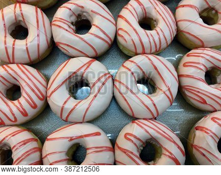 Row Of Donut Coating White Chocolate And Topped With Strawberry Cream. It Is A Small Fried Cake Of S