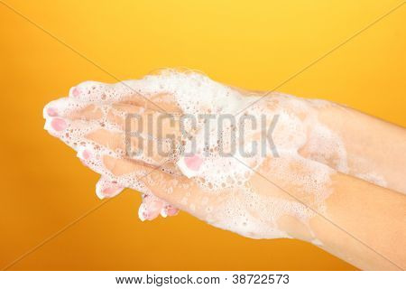 มือของผู้หญิงใน soapsuds บนพื้นหลังสีส้มอย่างใกล้ชิด