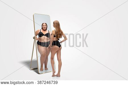 Young Fit, Slim Woman Looking At Fat Girl In Mirrors Reflection On White Background. Thinking Shes N