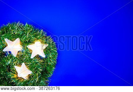 Three Stars Shaped Christmas Lights  With The Green And Gold Tinsel, Isolated On The Blue Background