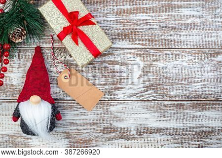 Christmas Composition With Pine Branch, Gift Box, Shopping Tag And Gnome Or Swedish Tomte, On A Wood