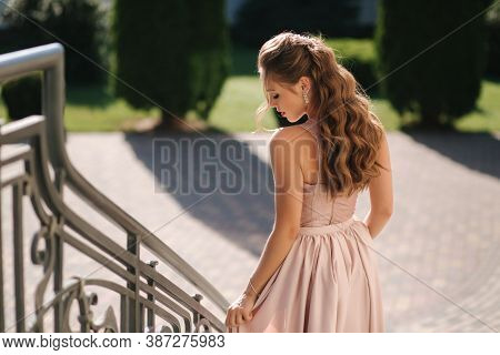 Attractive Young Woman In Gorgeous Evening Dreess And Curly Hair Posing To Photographer