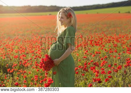 Beautiful Blonde Pregnant Woman In Long Green Dress With A Bunch Of Flowers In Hand, In The Middle O