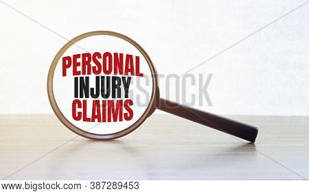 Magnifying Glass With Text Personal Injury Claims On Wooden Table.