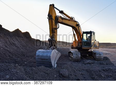 Excavator During Excavation At Construction Site On Sunset Background. Red Backhoe On Road Work. Hea