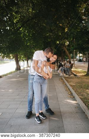 Handsome Man With His Gorgeous Girlfriend. Happy Couple Walking Along The Embabkment. Green Backgrou