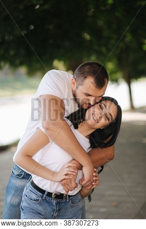 Handsome Man With His Gorgeous Girlfriend. Happy Couple Walking Along The Embabkment. Green Backgrou