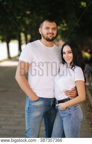Handsome Man With His Gorgeous Girlfriend. Happy Couple Walking Along The Embabkment. Green Backgrou