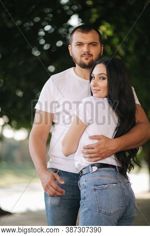 Handsome Man With His Gorgeous Girlfriend. Happy Couple Walking Along The Embabkment. Green Backgrou