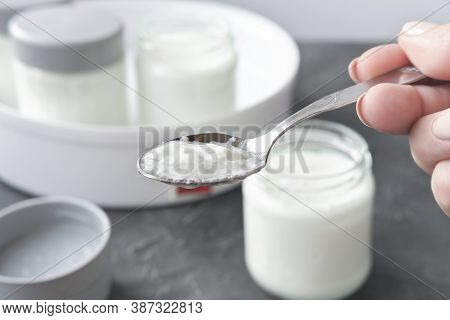 Female Hand Holding A Spoon With Kefir Or Yogurt Made In Automatic Yoghurt Making Machine. Fermented