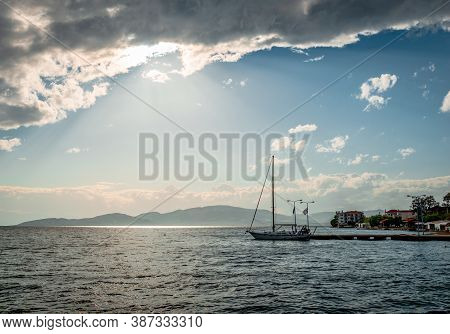 A Sailboat In The Sunset. Dark Clouds In Blue Sky. In Agria, Greece.