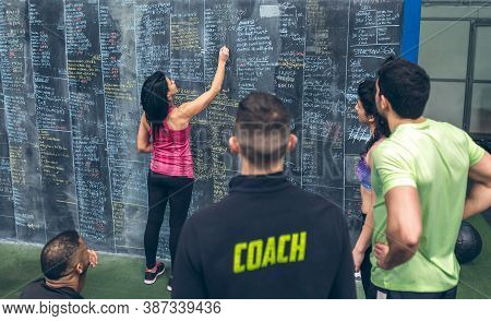 Athlete Woman Writing Down Results On The Gym Blackboard With Her Classmates And Coach