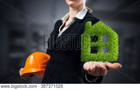 Real Estate Agent Holds In Palm Green Plant In Shape Of House. Woman In Business Suit With Safety He