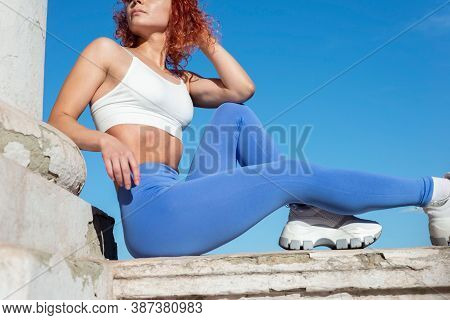Red-haired Woman Athlete, Thirty-six Years Old, In Sports Leggings, Sits On The Street, Demonstratin