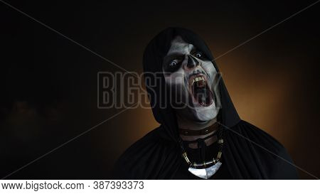 Creepy Man With Skeleton Makeup In Hood. Guy Executioner Making Angry Faces, Looking At Camera Tryin