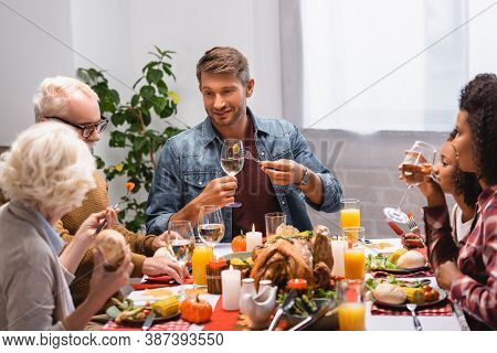 Focus Of Man Holding Wine Near Multiethnic Family During Thanksgiving Ginner At Home