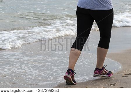 Rear View Of A Runner Is Running On The Hard Sand Close To The Ocean Wearing Spandex.