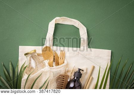 Zero waste concept. Cotton bag, bamboo cultery, glass jar, bamboo toothbrushes, hairbrush and straws on green background