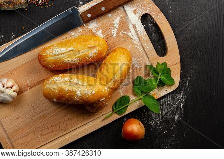 Fresh Wheat White Bread On A Cutting Board With Seasonings Sprinkled With Flour On A Black Wooden Ta