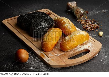 Fresh Black Rye And White Bread On A Cutting Board With Seasonings Sprinkled With Flour On A Black W