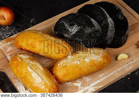 Fresh Black Rye And White Bread On A Cutting Board With Seasonings Sprinkled With Flour On A Black W