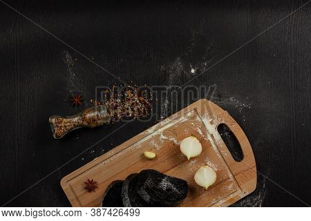 Fresh Black Rye Bread On A Cutting Board With Seasonings Sprinkled With Flour On A Black Wooden Tabl