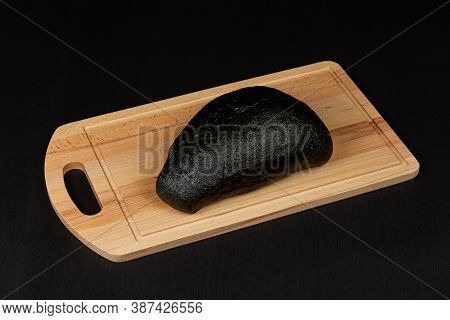 fresh black rye bread on a cutting board with seasonings sprinkled with flour on a black wooden tabl