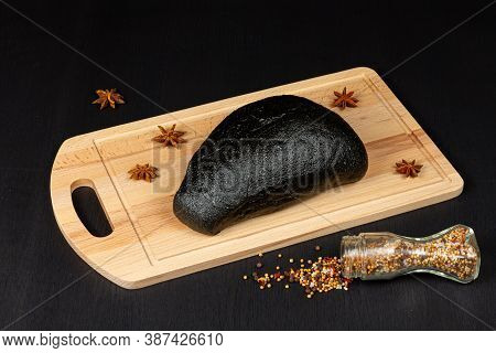 fresh black rye bread on a cutting board with seasonings sprinkled with flour on a black wooden tabl